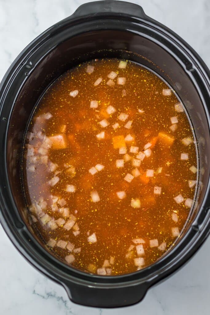 Vegetables being added to a crock pot.