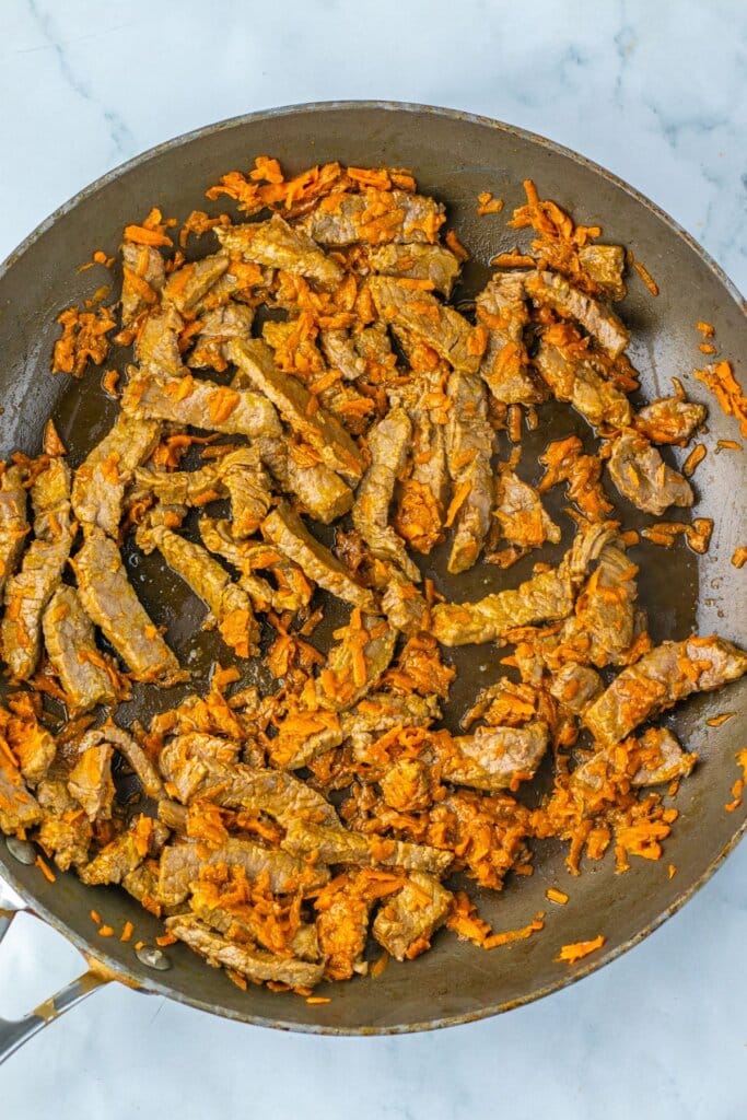 Meat and carrots being cooked in a skillet.