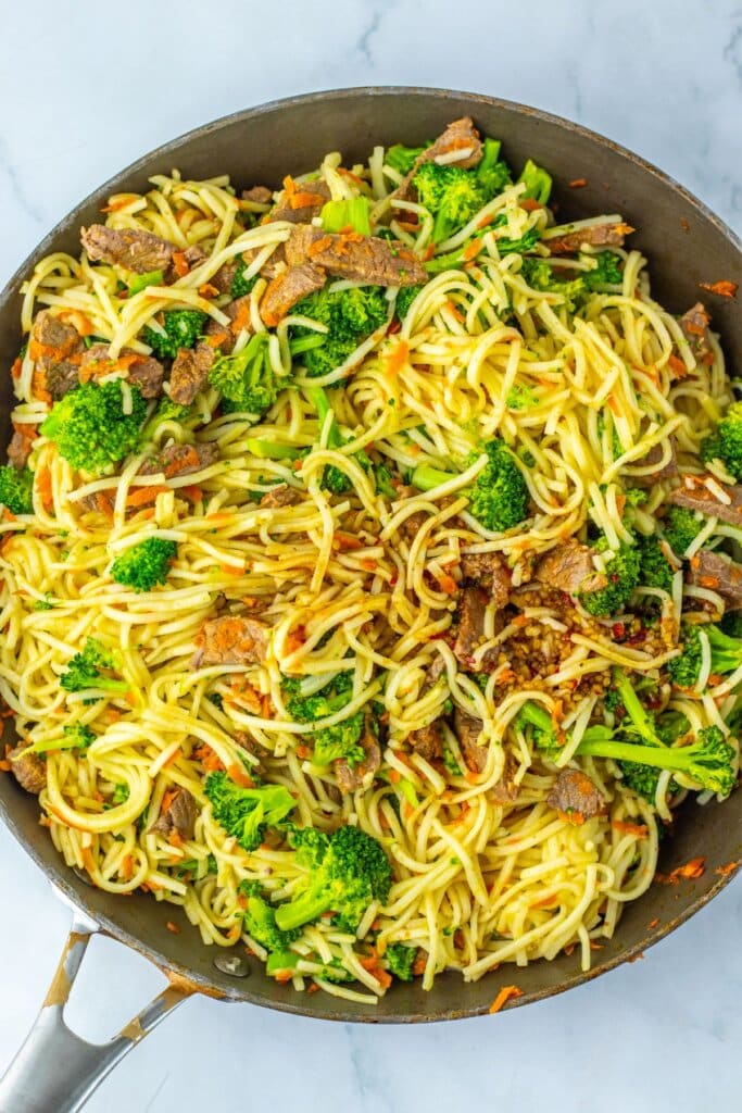 Noodles and meat being mixed in a skillet.