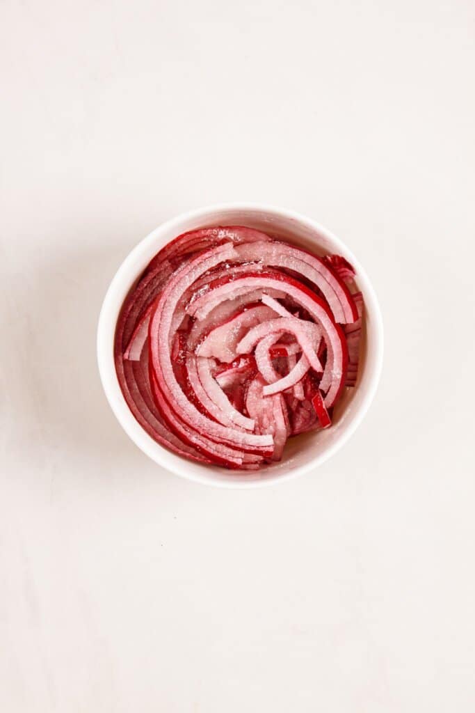 Red onions being pickled in a small bowl.