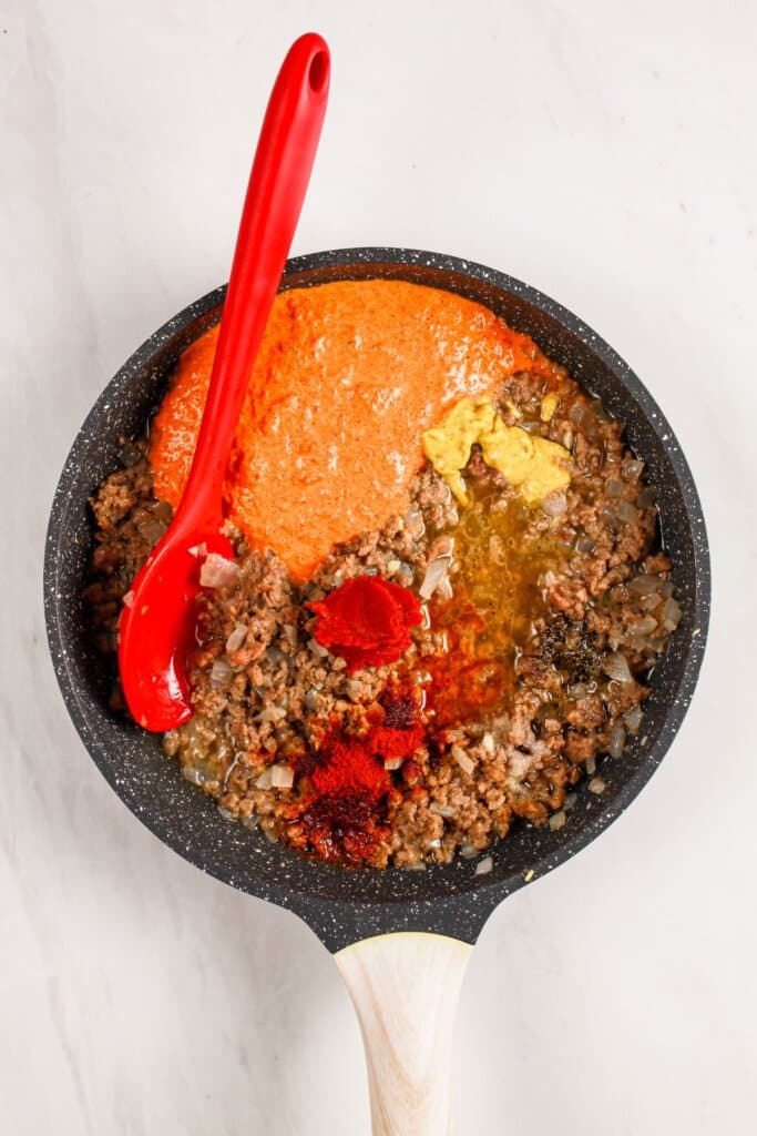 Sauce being added to cooked ground beef in a skillet.