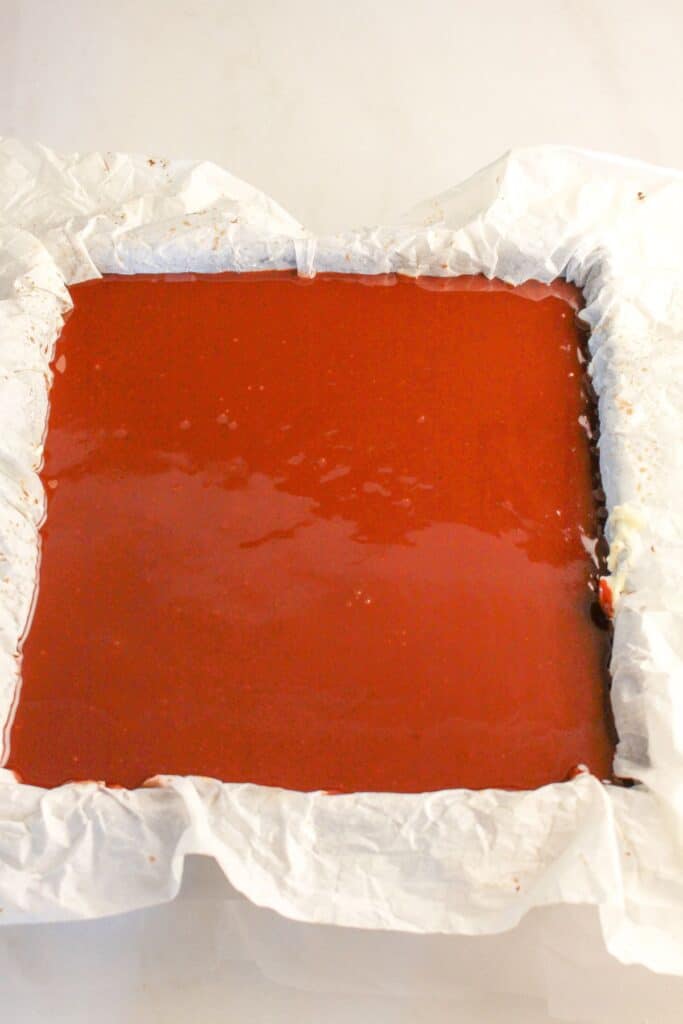 Ganache being spread on top of dessert in a baking pan.