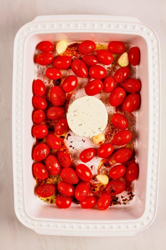 Cheese wheel, garlic, and vegetables in a baking dish.
