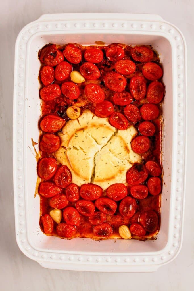 Cooked vegetables and cheese wheel in baking dish.