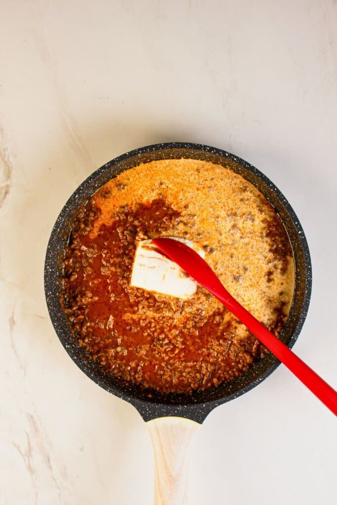 Beef, seasoning and cream cheese being cooked in a skillet.