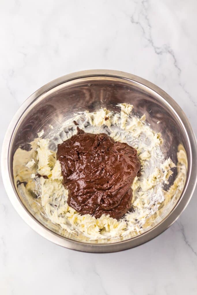 Chocolate being added to butter and sugar in a mixing bowl.