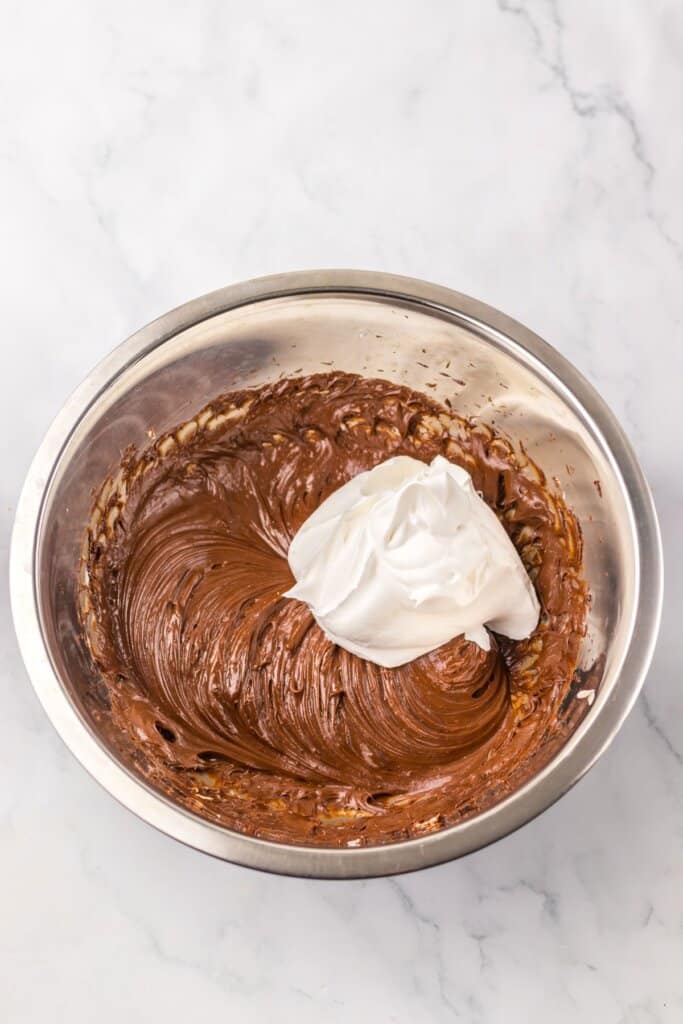 Whipped topping being added to batter in a mixing bowl.