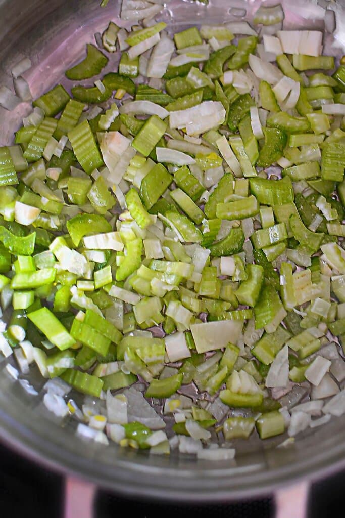 Celery and onions cooking in a pot on the stove.