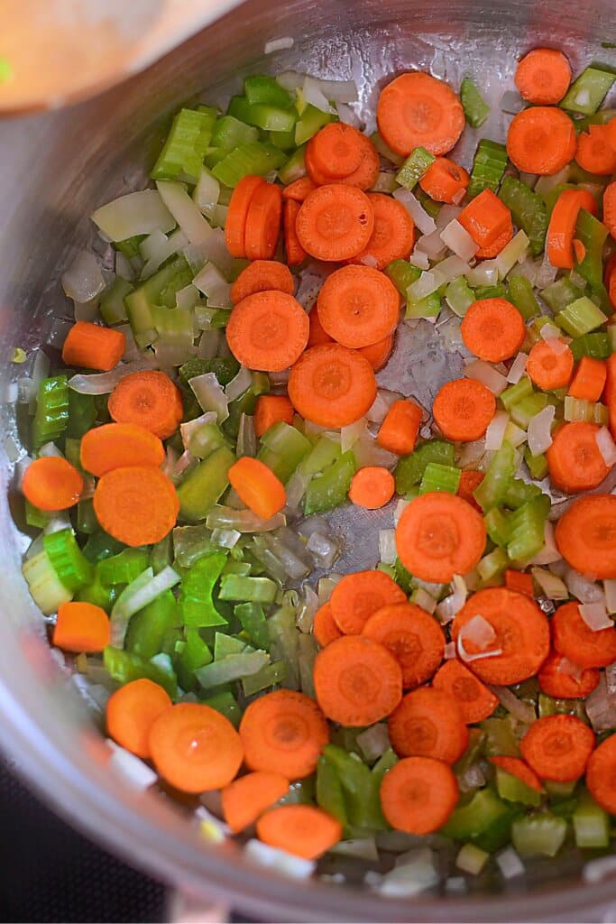 Celery, carrots and onions in a pot on a stove.