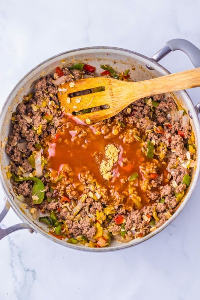 Sauce being added to cooked meat in a skillet.