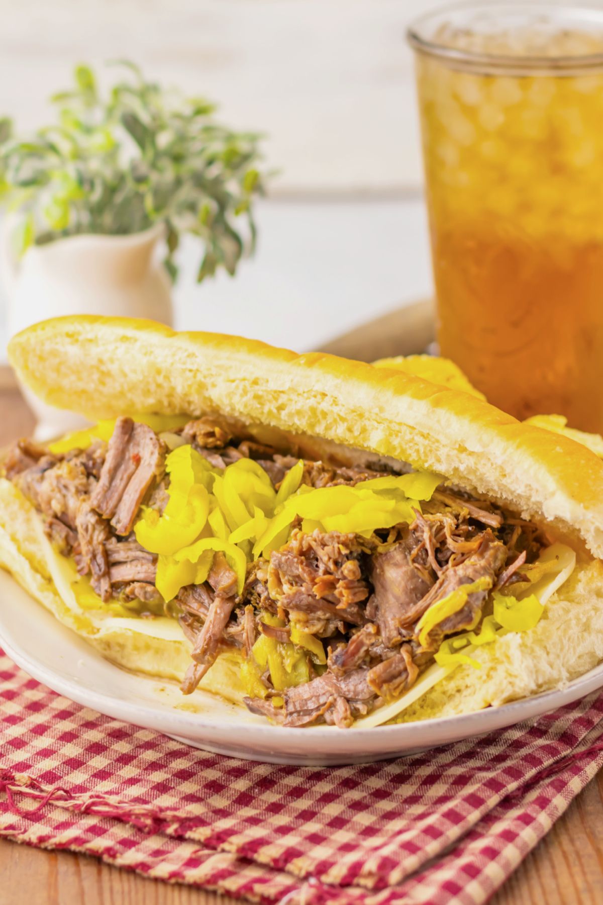 Italian beef sandwich on a hoagie roll topped with giardiniera peppers on a red checkered cloth.