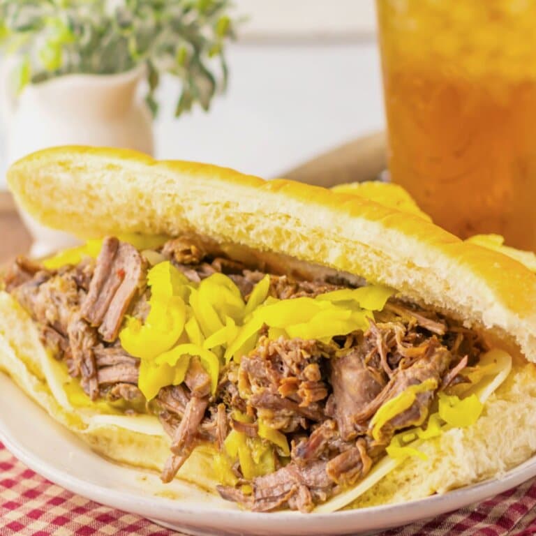 Close-up of a slow cooker Italian beef sandwich with tender shredded beef and giardiniera peppers on a hoagie roll.