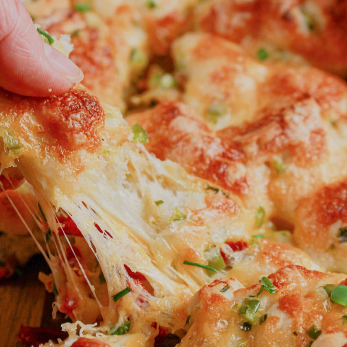 Piece of pull apart bread being removed from a cutting board.