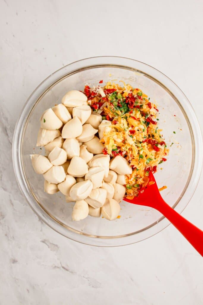 Dough balls being mixed with ingredients in a glass bowl.