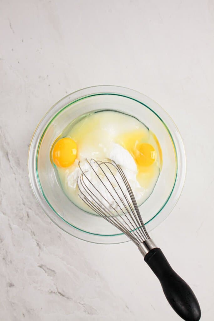 Eggs and sugar being mixed together in a glass bowl.