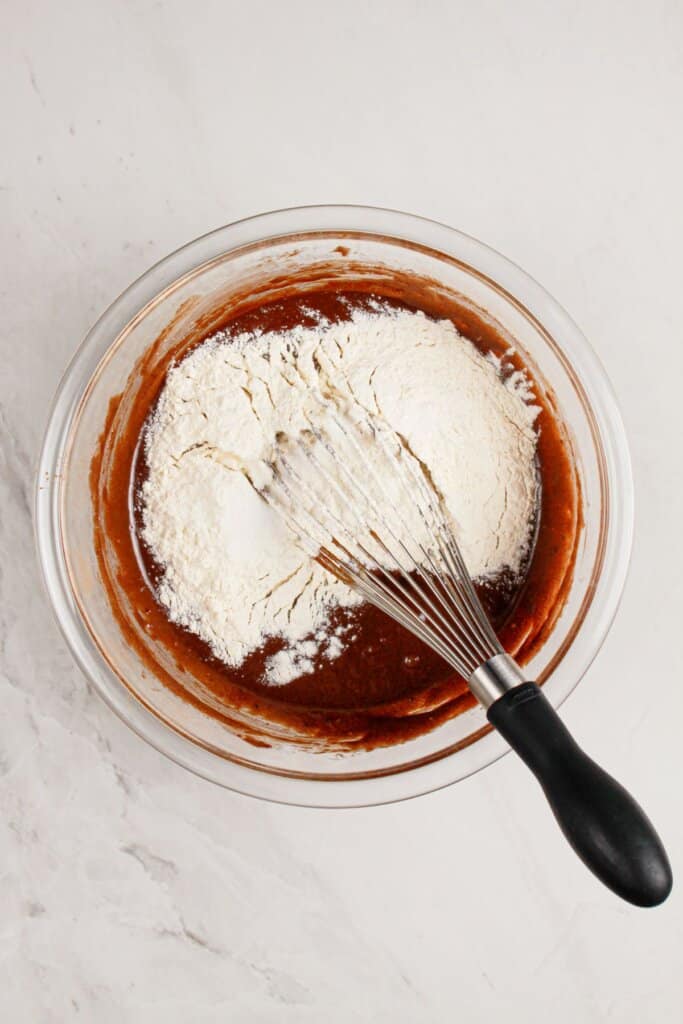 Dry ingredients being added to batter in a glass bowl.
