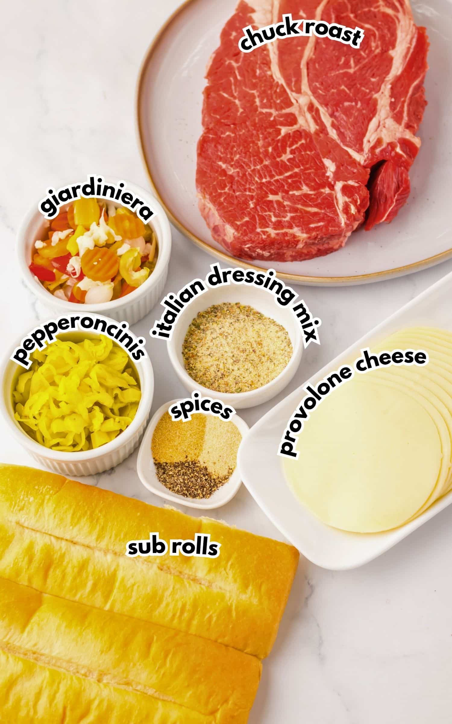 Ingredients for slow cooker Italian beef sandwiches including chuck roast, giardiniera, pepperoncinis, Italian dressing mix, spices, provolone cheese, and sub rolls.