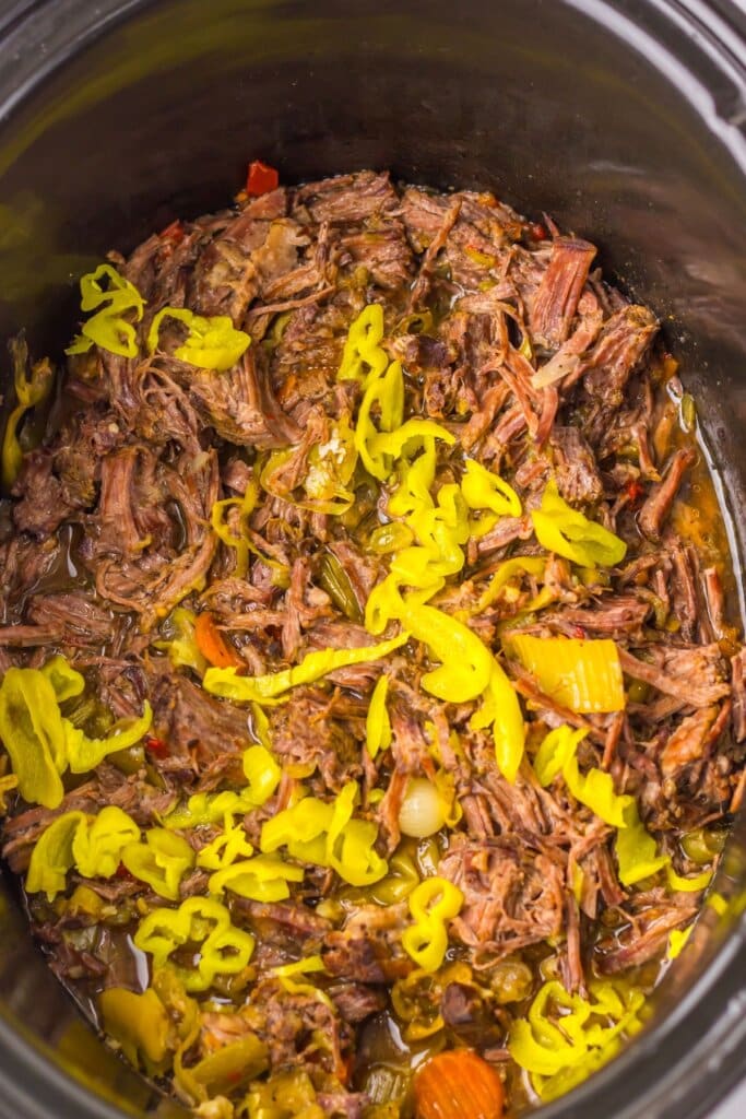 Shredded Italian beef with pepperoncinis and vegetables cooking in a slow cooker.