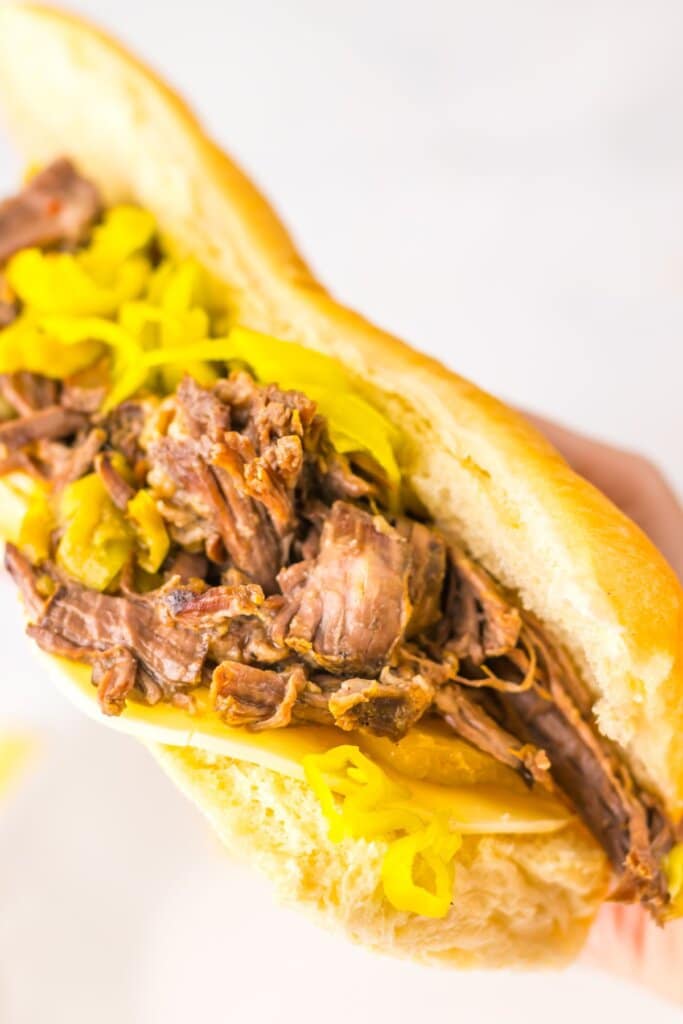 Close-up of a slow cooker Italian beef sandwich showing tender shredded beef and giardiniera peppers overflowing from a hoagie roll.