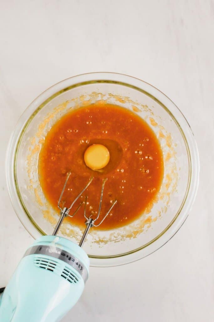 Eggs being mixed into batter in a glass bowl.