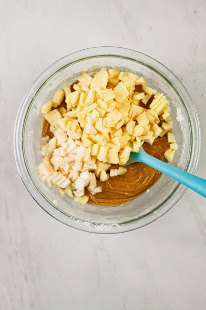 Fruit being stirred into batter in a glass bowl.