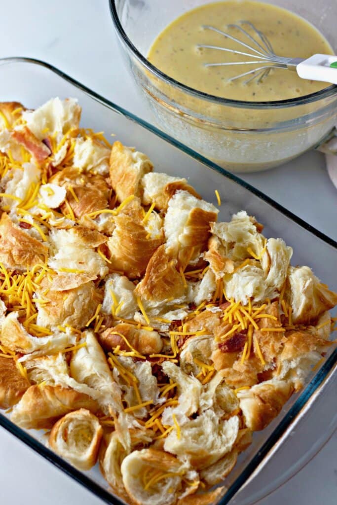 Bread pieces and shredded cheese in a glass baking dish.
