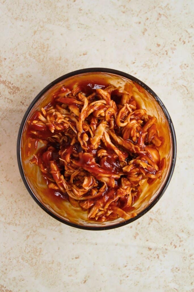 Meat being mixed with barbecue sauce.