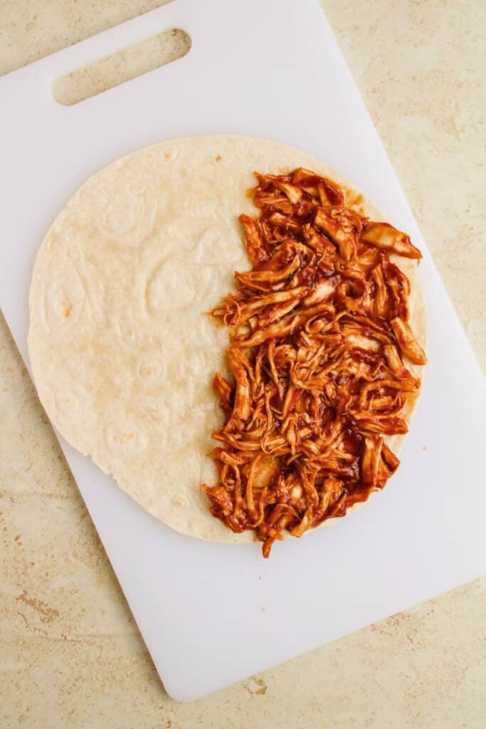 Meat being layered on top of a tortilla.