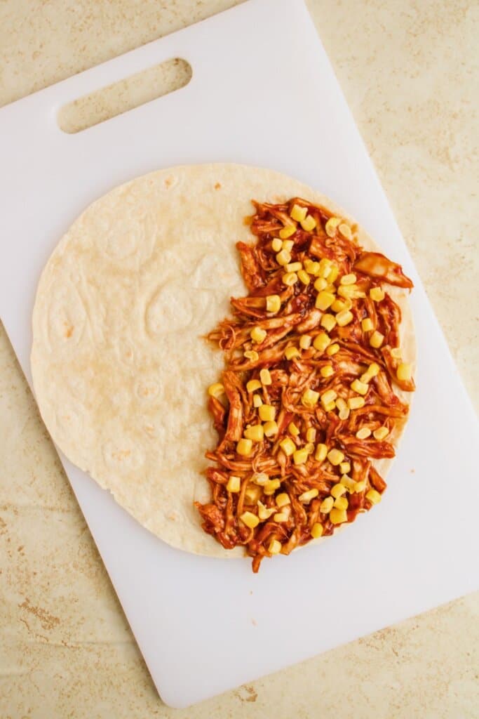 Corn being added to the top of a tortilla.