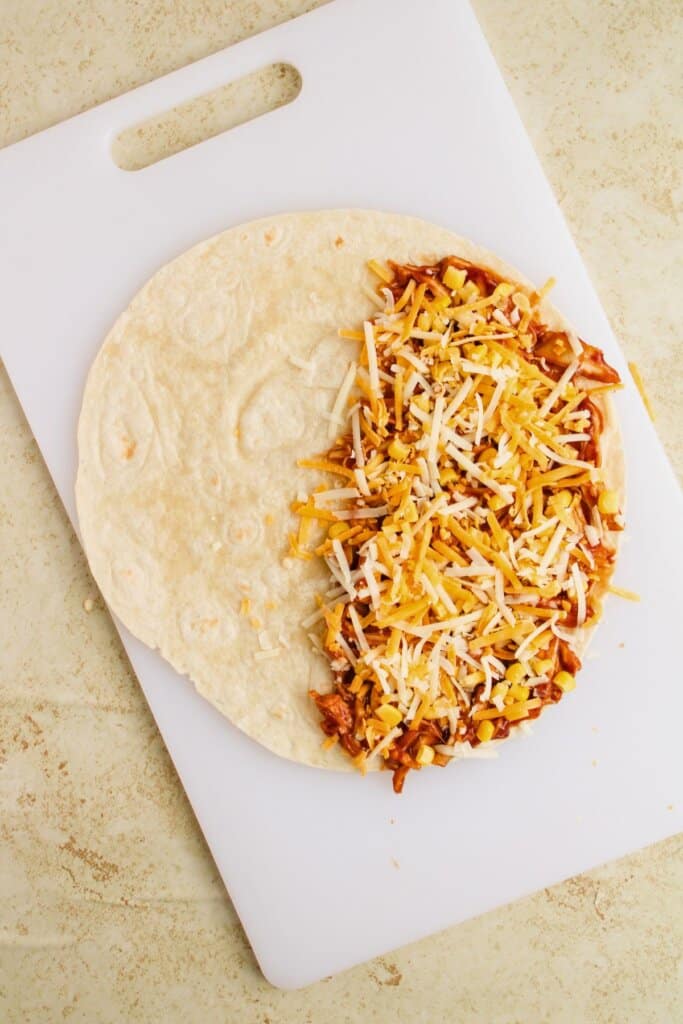 Cheese being sprinkled on meat on a tortilla.