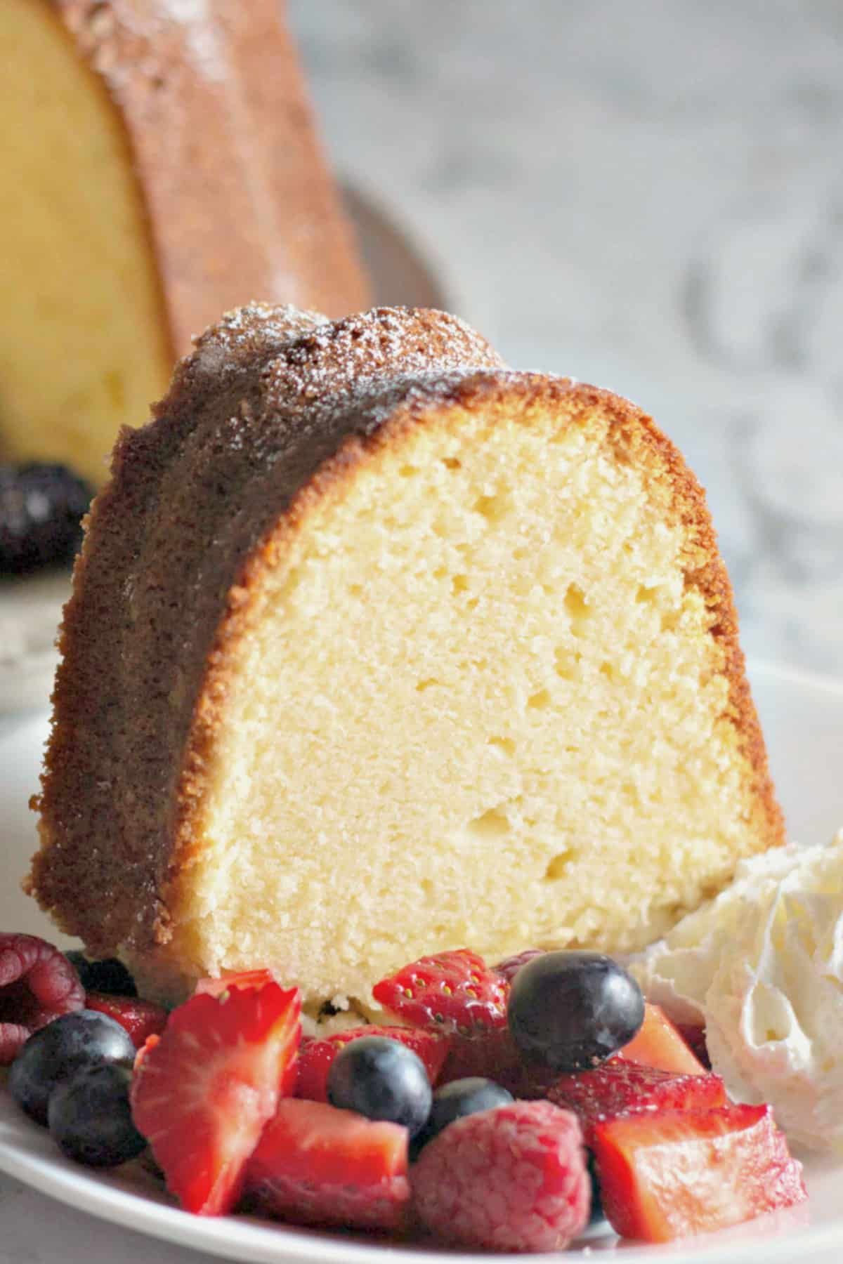 Slice of pound cake on a small plate with berries and whipped cream.
