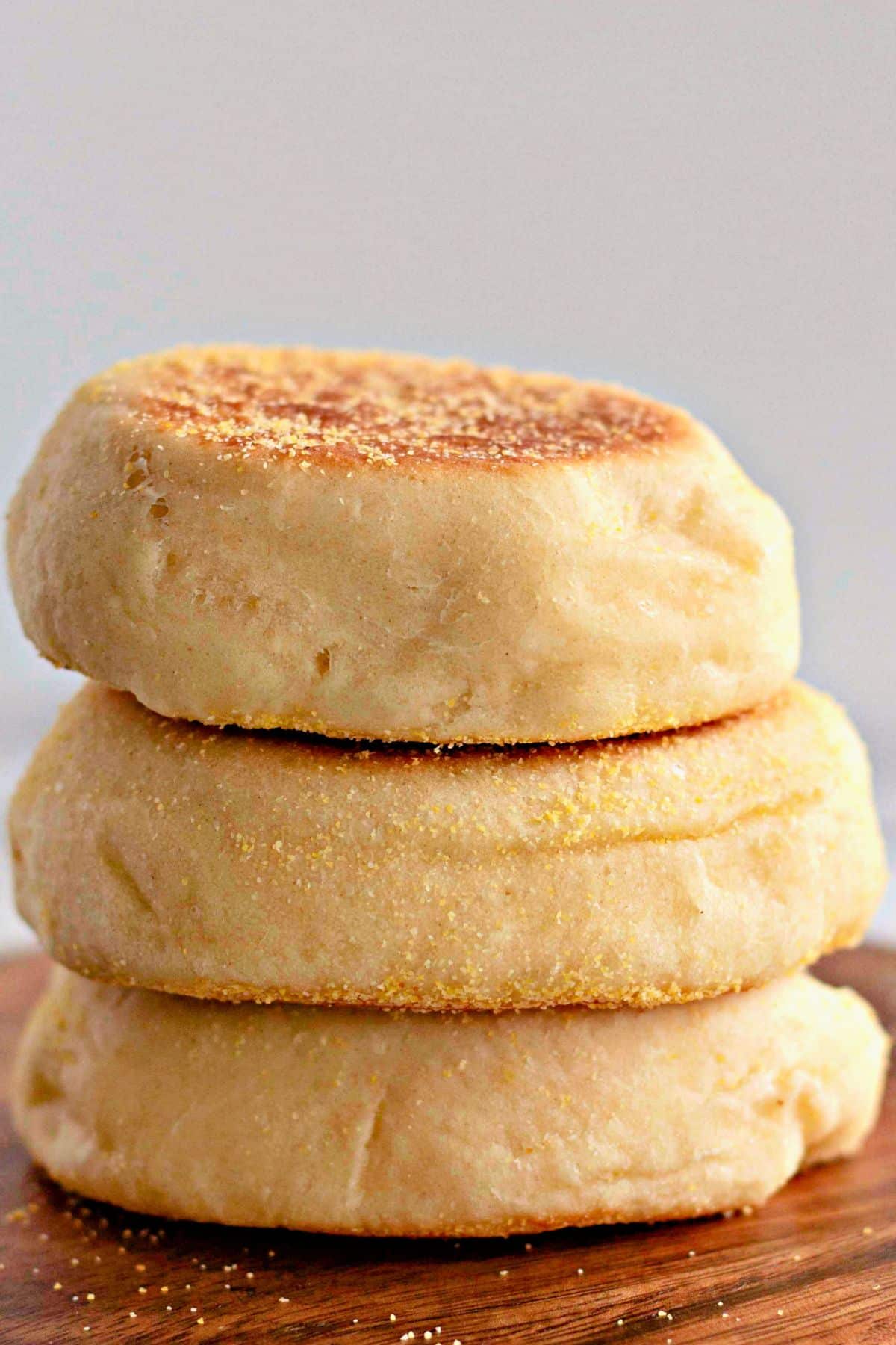 Three homemade english muffins on a cutting board.