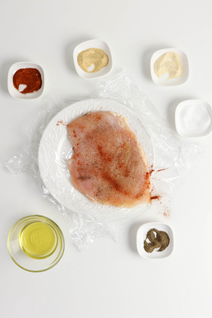 Adding the seasonings to the thin chicken breast.