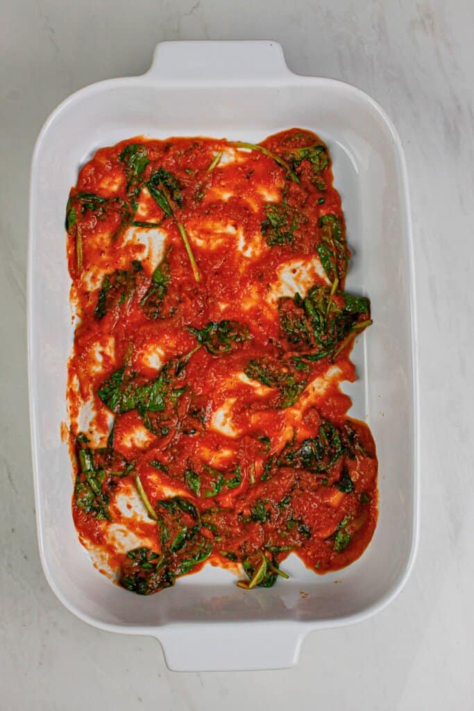 Sauce and spinach in a baking dish.