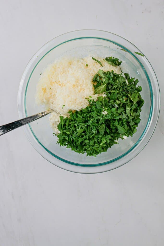 Ricotta, parmesan, and basil being mixed in a small bowl.