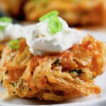 Onion fritter topped with sour cream on a small white plate.