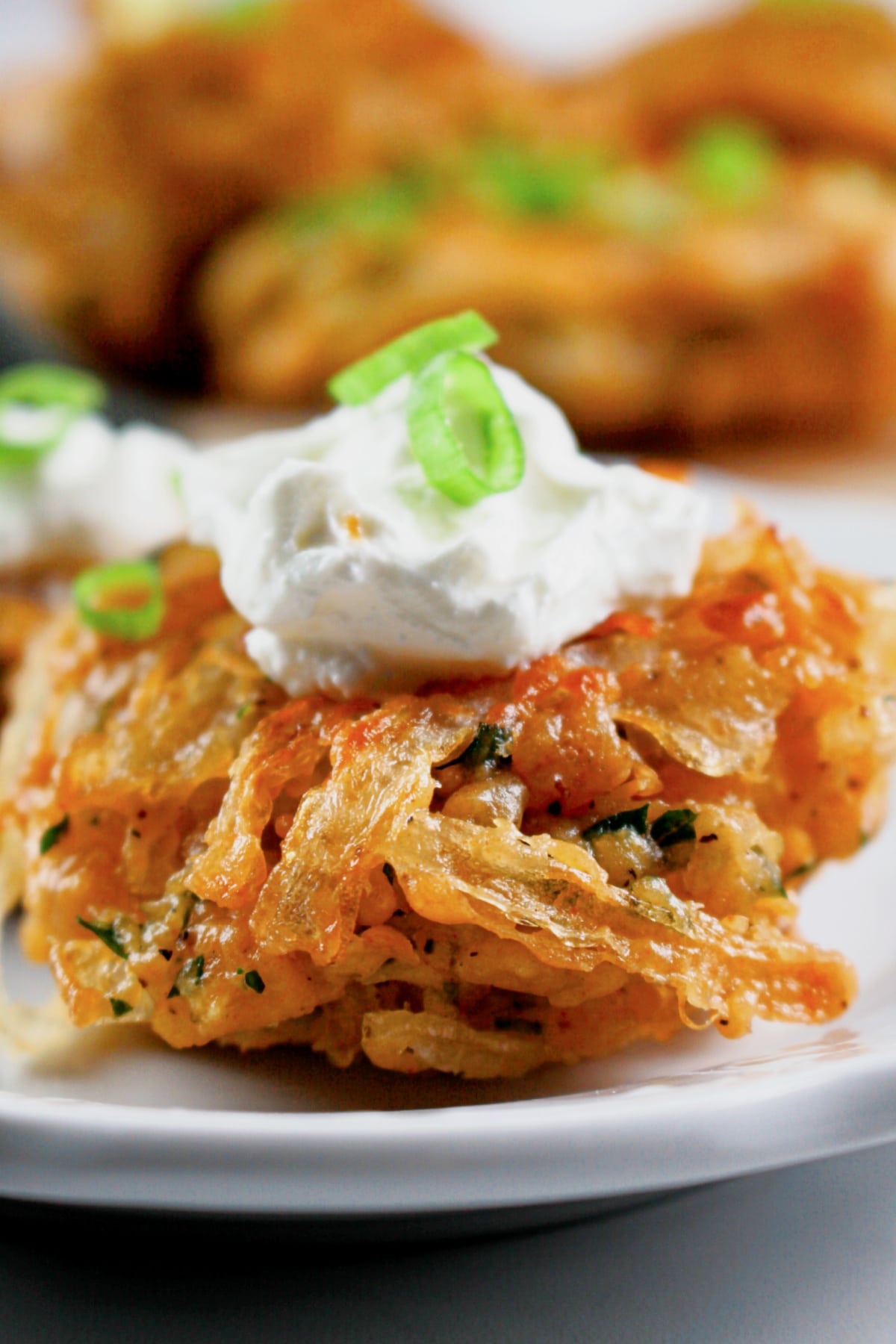 Onion fritter topped with sour cream on a small white plate.