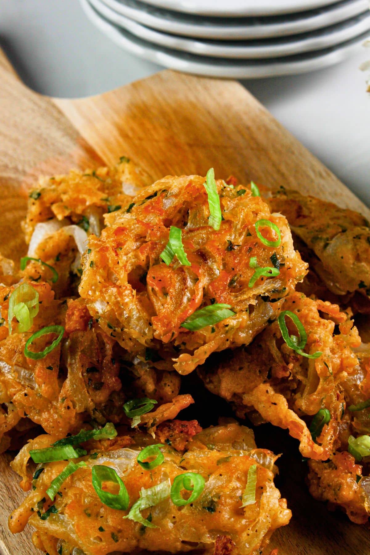 Onion fritters stacked in a pyramid on a wooden cutting board.