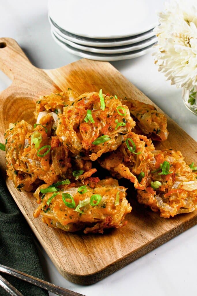 Onion fritters stacked in a pyramid on a wooden cutting board.