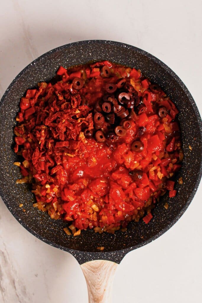 Tomatoes and olives cooking in a skillet.