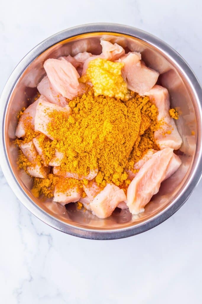 Meat being seasoned in a mixing bowl.