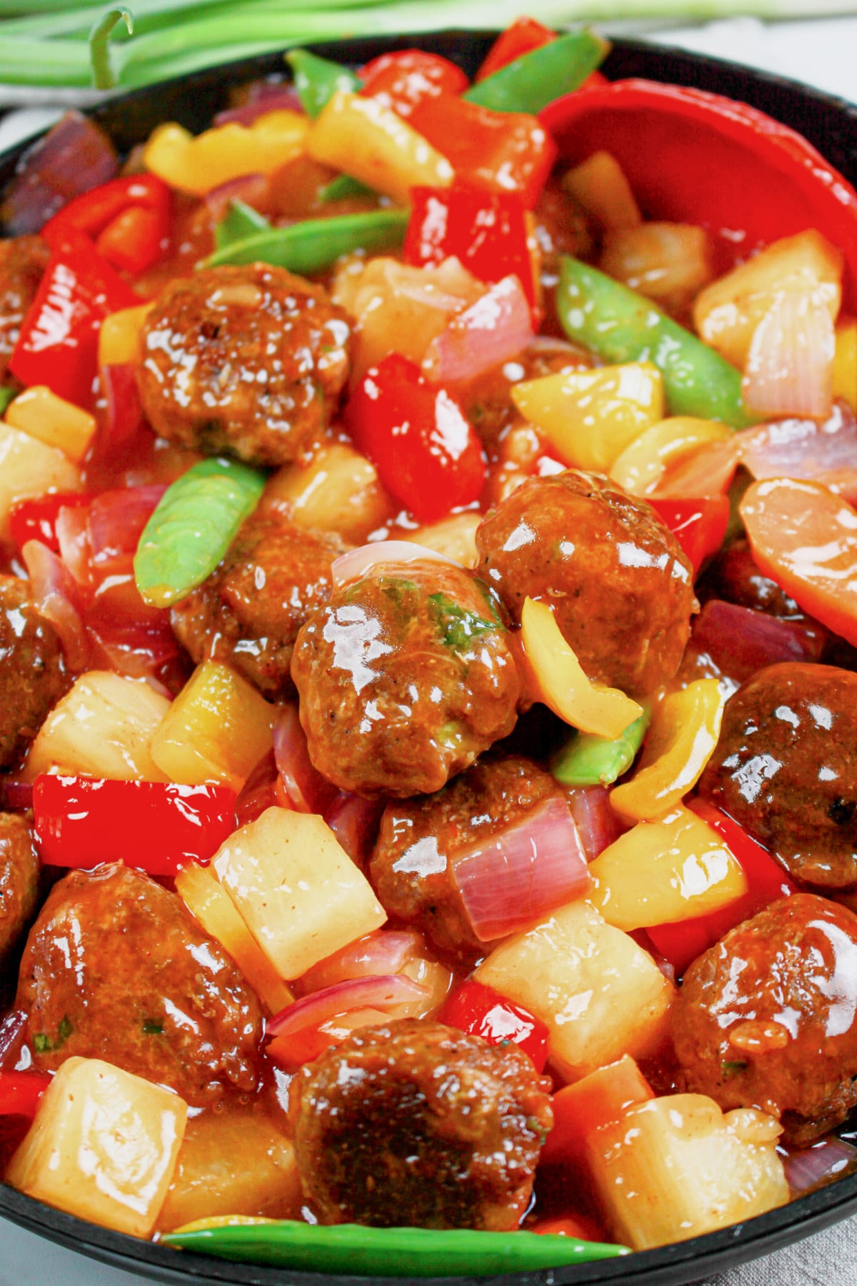 Skillet full of sweet and sour meatballs and veggies.