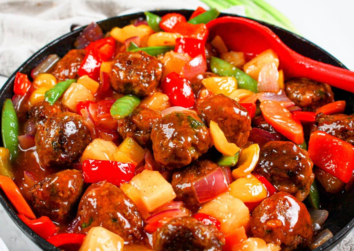 Skillet full of sweet and sour meatballs and veggies.