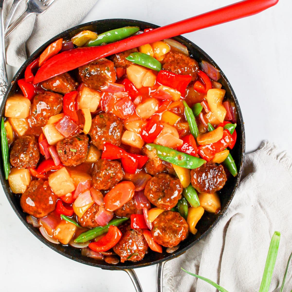 Skillet full of sweet and sour meatballs and veggies.
