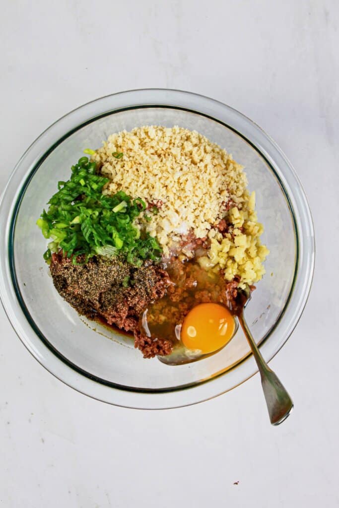 Ground beef and filling ingredients being mixed in a glass bowl.