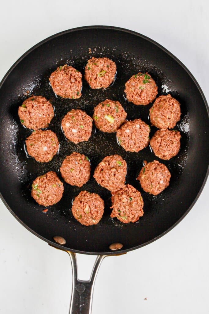 Ground beef balls being cooked in a skillet.